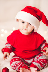 Cute baby sitting in bed wearing santa claus hat and suit. Looking at camera. Holiday season. Childhood.