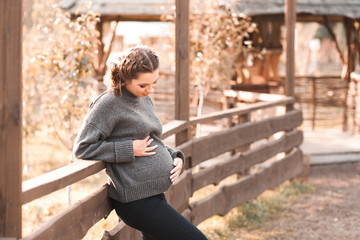 Beautiful pregnant woman wearing cozy knitted sweater holding tummy at countryside. Maternity....