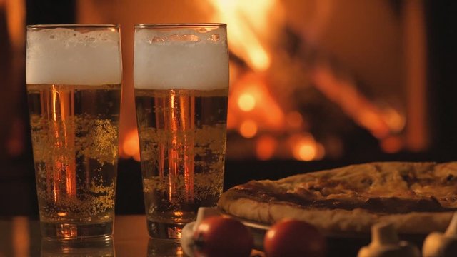Cinemagraph - Two glasses of beer and pizza over fireplace background. Motion Photo.