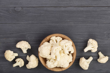 Fresh cauliflower cut into small pieces in wooden bowl on black background with copy space for your text. Top view