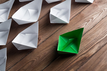 Business leadership concept with white and color paper boats on wooden table
