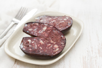 smoked sausage morcela on white dish on wooden background