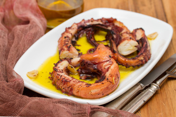 grilled octopus with garlic on white dish on wooden background