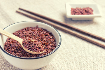 Close up of raw red brown rice on a wooden spoon in a white cera