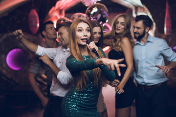 A woman in a green dress is singing songs with her friends at a karaoke club. Her friends have fun...