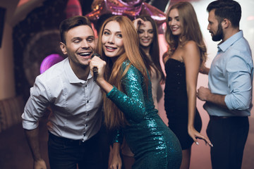 A woman in a green dress is singing songs with her friends at a karaoke club. Her friends have fun on the background.