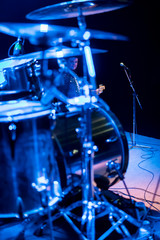 Bass guitarist behind drums at a concert in blue light