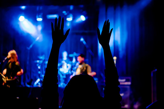 Silhouette of female hands raised at a rock concert in front of the stage with musicians