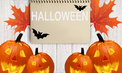 carved pumpkins for a Halloween and a notepad for writing on a wooden table with yellow leaves. - 181540184