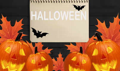 carved pumpkins for a Halloween and a notepad for writing on a wooden table with yellow leaves. - 181540744