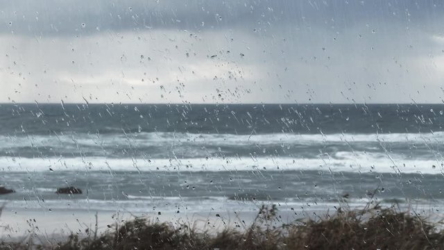 Real time scenic of rain falling at stormy ocean coast looking out through glass pane.