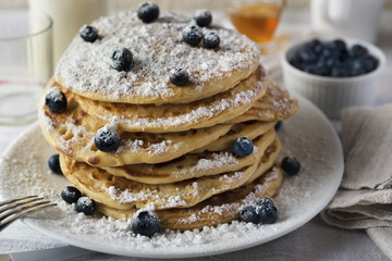 Tasty breakfast of pancakes with blueberries, powdered sugar, milk and honey in a white plate