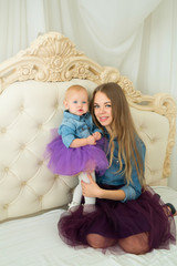beautiful happy mother with little daughter in jeans attire on a light bed