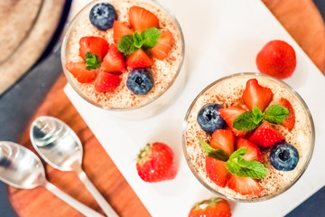 Homemade italian dessert tiramisu with strawberrie, blueberry, mint in glass jars, top view on a white background