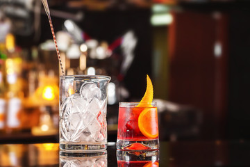 Closeup glass of negroni cocktail decorated with citrus and decanter with ice at bar stand festive...