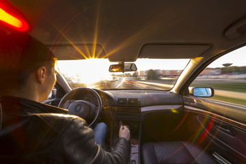 Driver's hands on steering wheel inside of a car and sunset sun with lens flare