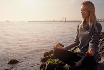 Say NO to depression this autumn. Young woman in warm clothes meditating on stone on the beach on cold weather day