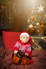 Little boy sitting and holding present in Santa Claus hat.