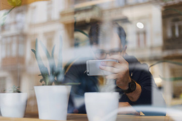 Young man using smartphone in a cafe. View through the window