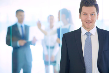 Portrait of young businessman in office with colleagues in the background . Portrait of young businessman.