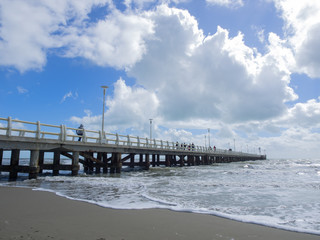 Fototapeta na wymiar Pleople walking on Forte dei Marmi's pier while big waves lurk on the beach