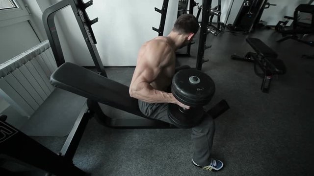 Athlete presses heavy dumbbells lying on the simulator in the gym.
