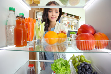 Portrait of female standing near open fridge full of healthy food, vegetables and fruits. Portrait of female