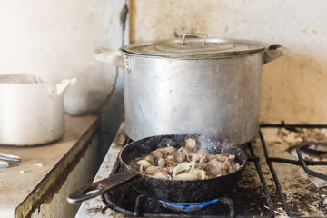 Pork meat frying in a frying pan on old an gas stove, closeup, retro 