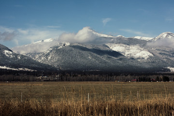 Snow covered mountain scene with bright blue sky over a grassy valley floor