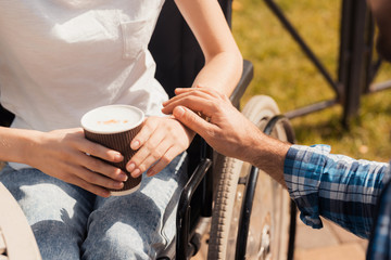 A couple of disabled people are drinking coffee while sitting at a table in the park.