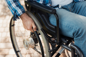 Close up. A disabled man in a wheelchair holds hands behind the wheelchair wheels.