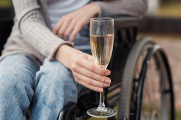 Close up. A woman in a wheelchair in the park holds a glass of champagne in her hands.