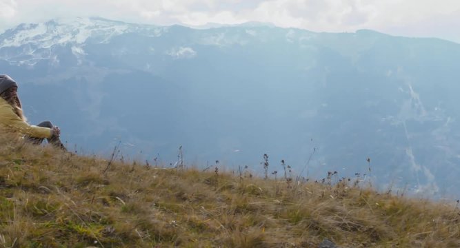 CRANE SHOT Caucasian female hiker in yellow raincoat wearing backpack halted on a scenic spot on the mountain top. 4K UHD RAW 60 FPS SLO MO