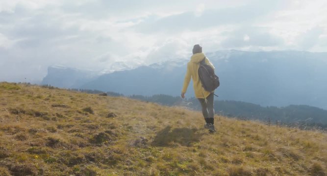 CU TO MED CRANE SHOT Caucasian female hiker in yellow raincoat wearing backpack halts on a scenic spot on the mountain top. 4K UHD RAW 60 FPS SLO MO
