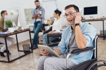 Disabled person in the wheelchair works in the office. He talks on smartphone.