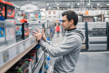 smart male customer buying car battery n the car supermarket. Difficult decision which battery to buy