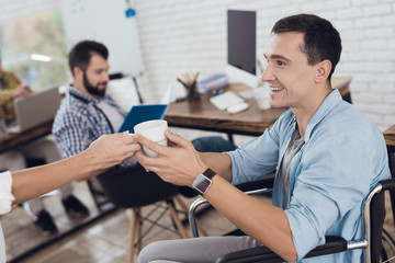 Obraz premium A girl gives a disabled in a wheelchair a cup of tea or coffee in a light modern office.