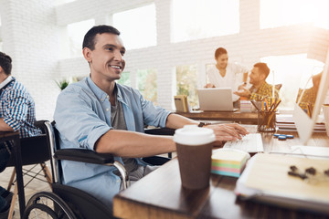 Disabled person in the wheelchair works in the office at the computer.