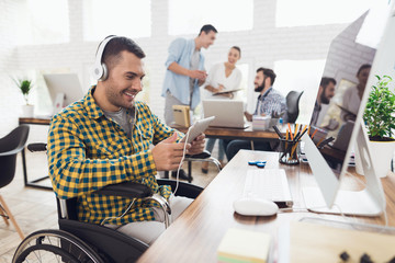 Obraz premium A man in a wheelchair works with a tablet and listens to music on headphones.