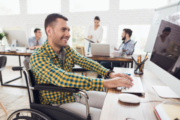 A man in a wheelchair is working the computer at a table in a modern office.
