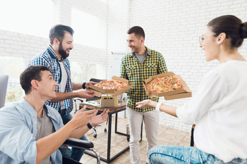 Office workers and man in a wheelchair are eating pizza. They work in a bright and modern office.