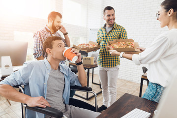 Office workers and man in a wheelchair are eating pizza. They work in a bright and modern office.