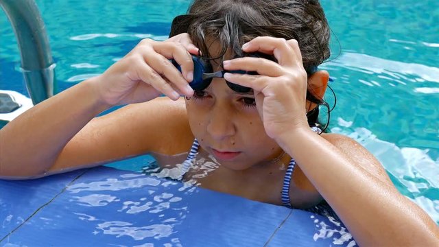 Portrait of a cute little girl with swimming glasses on the edge of a swimming pool, 4k