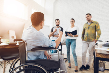 Fototapeta premium Mężczyzna na wózku inwalidzkim pokazuje dokumenty swojemu zespołowi w biurze. Pracują w jasnym, nowoczesnym biurze.