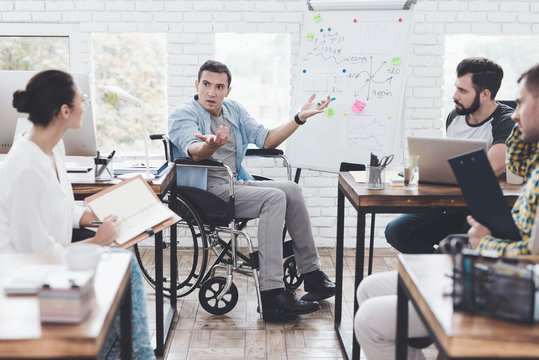 Office workers and man in a wheelchair discussing business moments in a modern office.