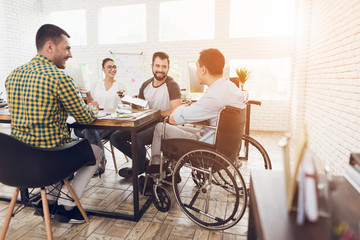 A man in a wheelchair communicates cheerfully with employees of the office during a business...