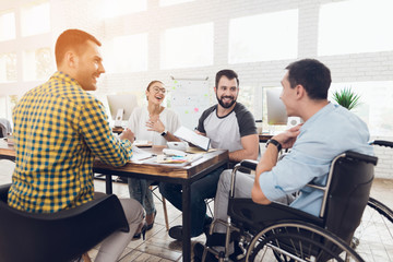 A man in a wheelchair communicates cheerfully with employees of the office during a business...