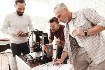 Three men set up a self-made 3d printer to print the form. They are preparing to launch the device for the first time.