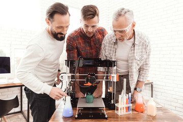 Three men are working to prepare printed on a 3d model printer. They stand three together around the 3d printert.