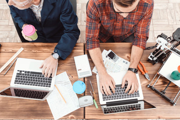 Two engineers are engaged in designing models for a 3d printer. They work on their laptops in the...